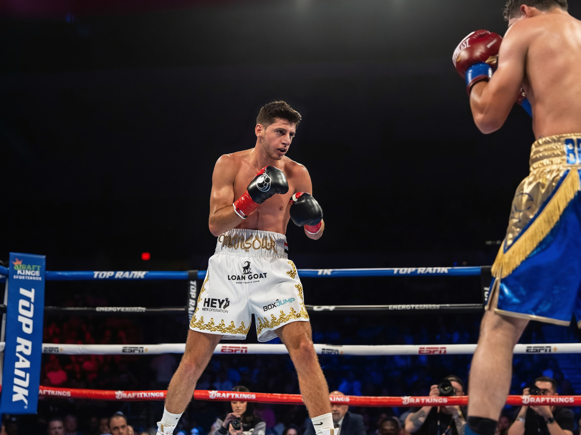 Jonny Mansour in the ring wearing sponsor-branded trunks